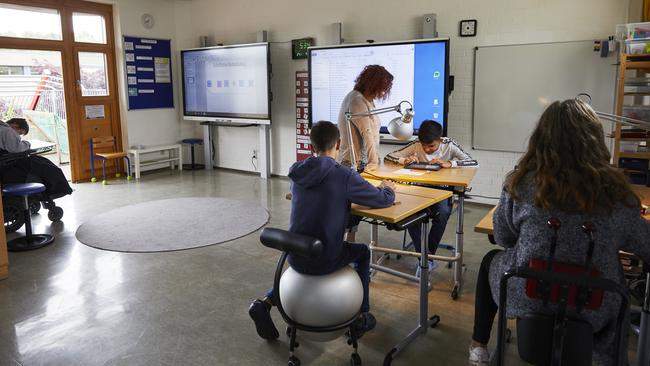 Ein Klassenraum mit einem Smartboard, einer Lehrerin sowie 4 Kindern, die an Tischen sitzen.