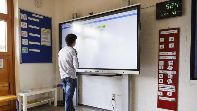 Eine Junge steht vor einem Smartboard und schaut darauf.
