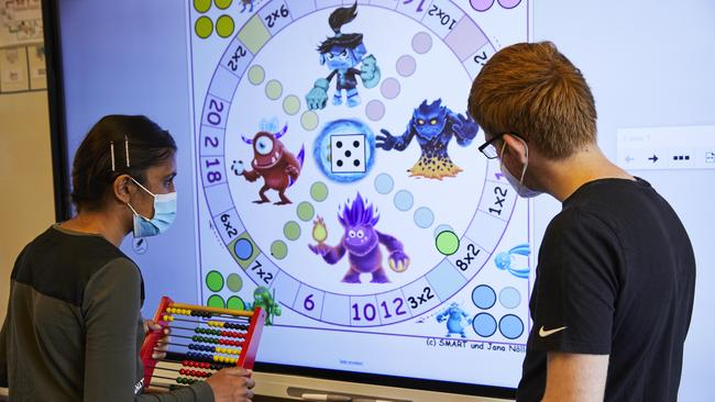 Zwei Jugendliche stehen vor einem Smartboard. Das Mädchen hat einen Rechenrahmen in der Hand.