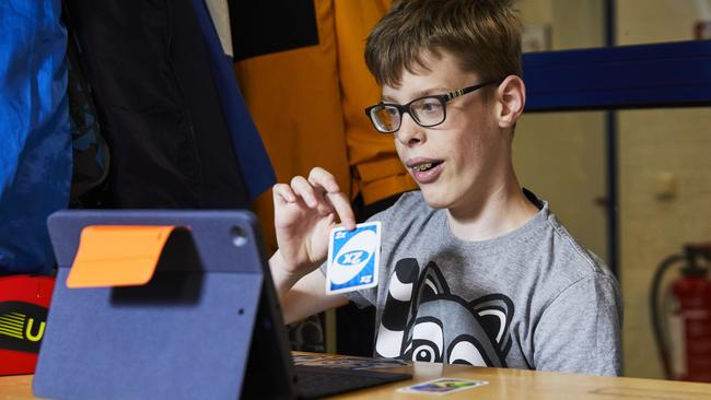 Ein Junge sitzt an einem Tisch vor einem iPad und hält eine Spielkarte in der Hand.