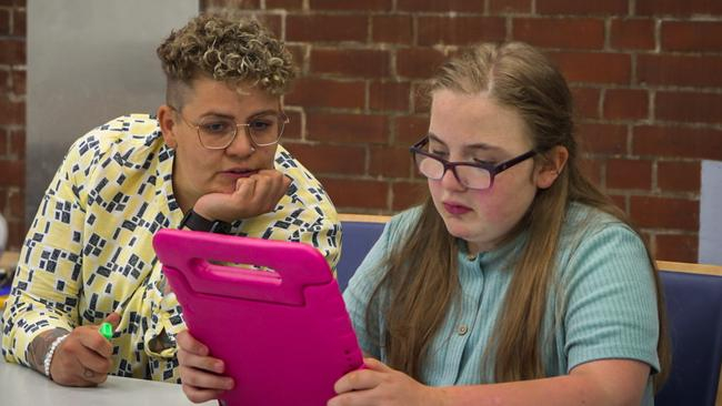 Eine Jugendliche sitzt an einem Tisch und schaut auf ein Tablet, das sie in der Hand hat. Bianca Rilinger sitzt neben ihr und schaut ebenfalls auf das Tablet.