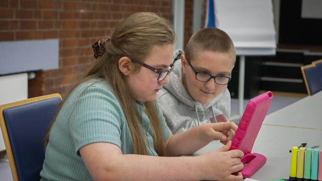 Zwei Jugendliche sitzen an einem Tisch und schauen gemeinsam auf ein Tablet.