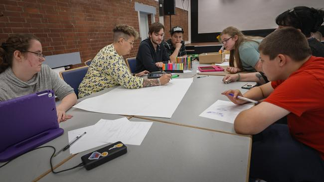 Mehrere junge Menschen sitzen an einem Tisch. Vor ihnen liegt ein großes, weißes Papier auf das sie schauen.