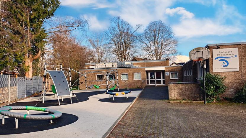 Blick auf ein Gebäude mit Flachdach. Im Vordergrund sind Klettergeräte und ein Trampolin zu sehen. Am Gebäude hängt ein  Schild mit der Aufschrift "inklusive OT Ohmstraße"