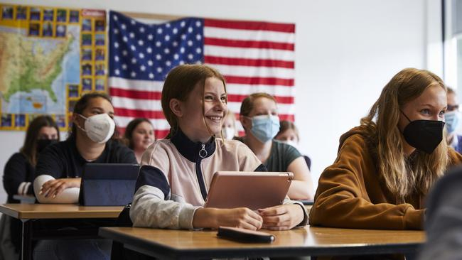 Ein Klassenraum von vorne. Einige Schüler*innen haben ein Tablet vor sich stehen. Im Hintergrund hängt eine Fahne der Vereinigten Staaten von Amerika.