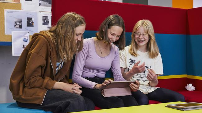 Drei Schülerinnen sitzen nebeneinander und schauen auf ein Tablet, das die Schülerin in der Mitte in der Hand hält. Alle drei lachen.