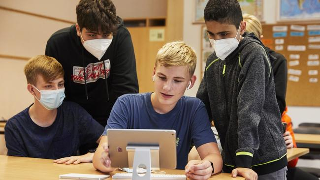 Mehrere Jugendliche stehe und sitzen um ein Tablet herum.