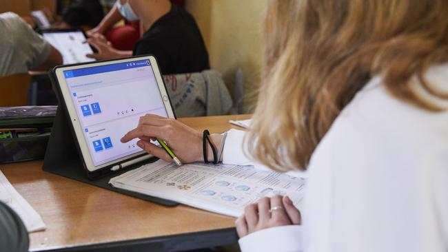 Eine Schülerin hat einen Ausdruck vor sich liegen, dahinter steht ein Tablet. Mit der rechten Hand berührt sie das Tablet.