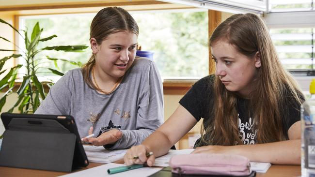 Zwei Schülerinnen sitzen nebeneinander am Tisch. Die eine schaut die andere an, während diese auf das Tablet schaut, das vor ihnen steht.