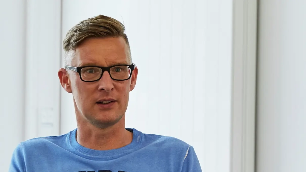 Lehrer Hauke Behrens sitzt an einem Tisch. Ihm Gegenüber und nur unscharf von hinten zu sehen ist eine weitere Person mit Laptop vor sich.