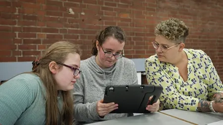 Zwei Jugendliche und Bianca Rilinger sitzen nebeneinander auf einer Bank. Sie alle schauen auf ein Tablet, dass das Mädchen in der Mitte in der Hand hält.