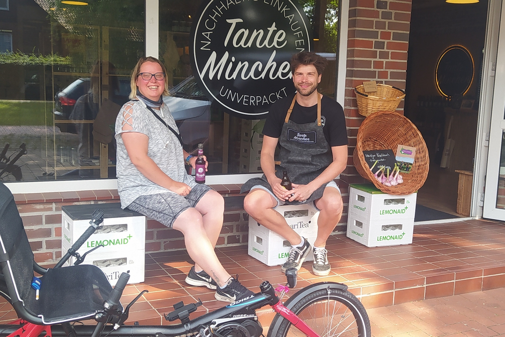 Eine Frau und ein Mann sitzen vor einem Laden und machen Pause. Im Vordergrund sieht man ein Spezialfahrrad.