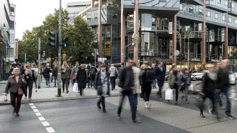 Menschen überqueren eine breite Straße in einer Innenstadt