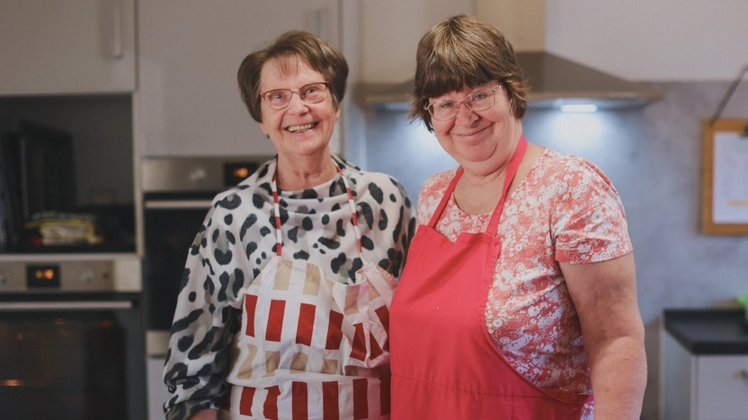 Zwei Frauen stehen nebeneinander in einer Küche. Sie lachen in die Kamera.