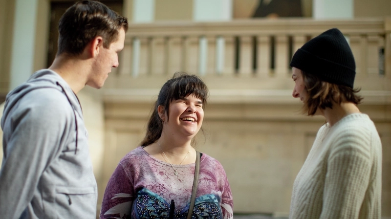 Carina unterhält sich in der Uni mit zwei Studenten und lacht.