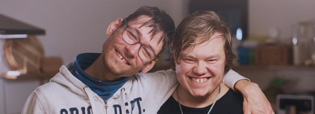 Zwei junge Männer mit geistiger Behinderung stehen lächeldn nebeneinander
