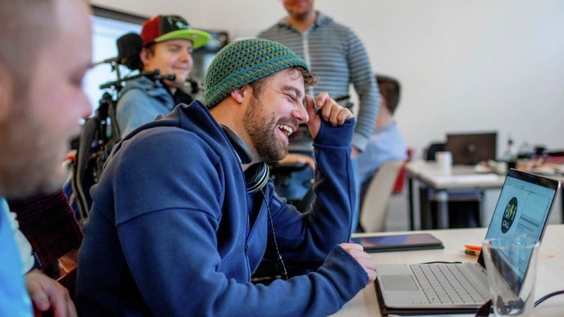 Ein Mann sitzt an einem Laptop und lacht.