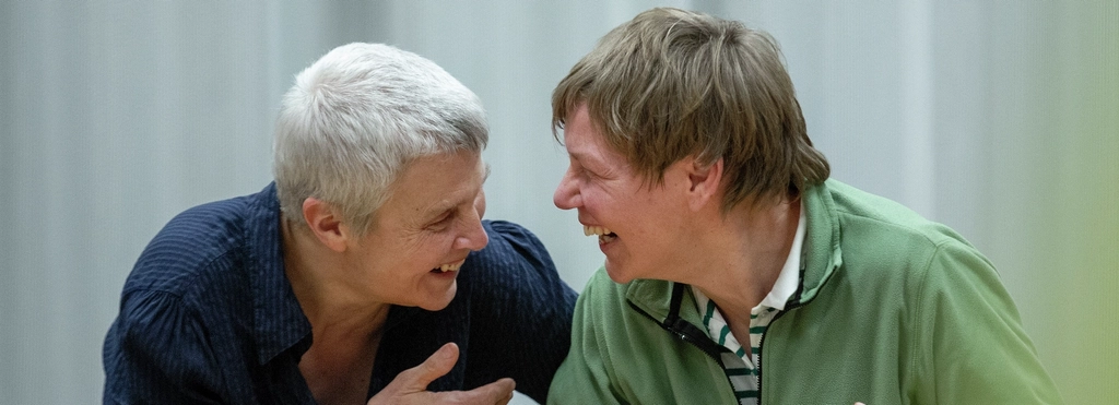 Zwei Frauen stehen Arm in Arm nebeneinander und lachen sich an