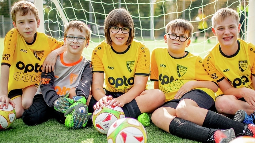 Fünf Jungen sitzen mit ihren Fußbällen auf dem Rasen und lächeln in die Kamera