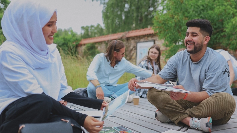 Vier Jugendliche sitzen gemeinsam auf einer hölzernen Terrasse und schauen Fotos an.