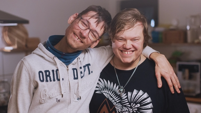 Zwei junge Männer mit geistiger Behinderung stehen lächeldn nebeneinander