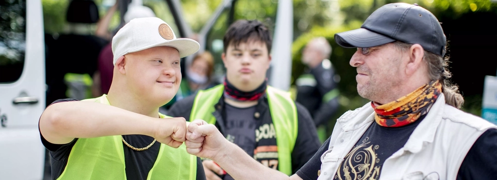 Ein Mann mit Downsyndrom begrüßt einen anderen Mann freundschaftlich mit einem Faust-Gruß. Beide gehören zu einem Motorradclub.