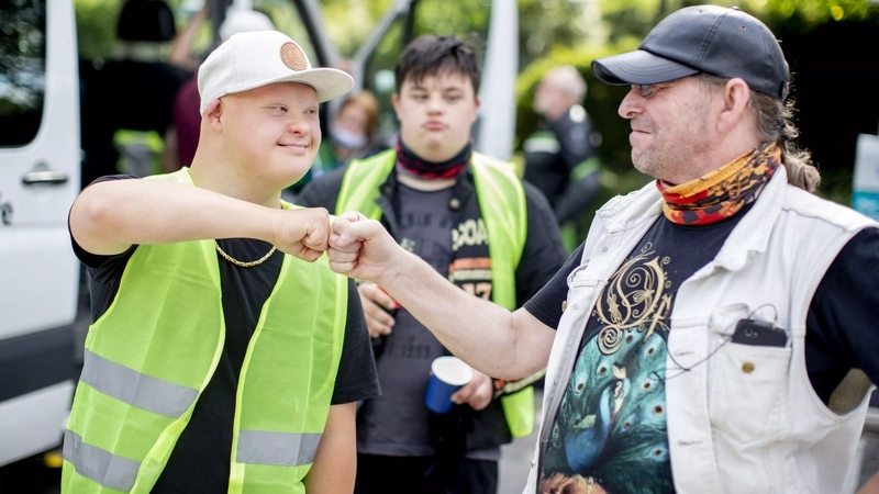 Ein Mann mit Downsyndrom begrüßt einen anderen Mann freundschaftlich mit einem Faust-Gruß. Beide gehören zu einem Motorradclub.