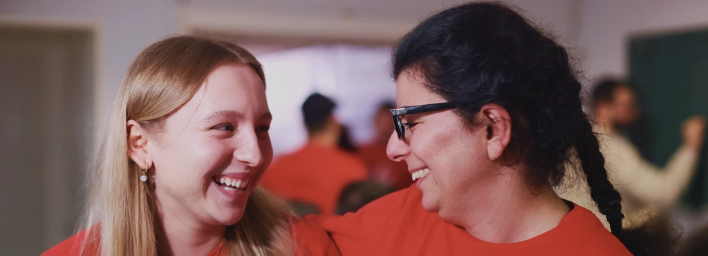 Zwei junge Frauen stehen Arm in Arm nebeneinander und lächeln sich an