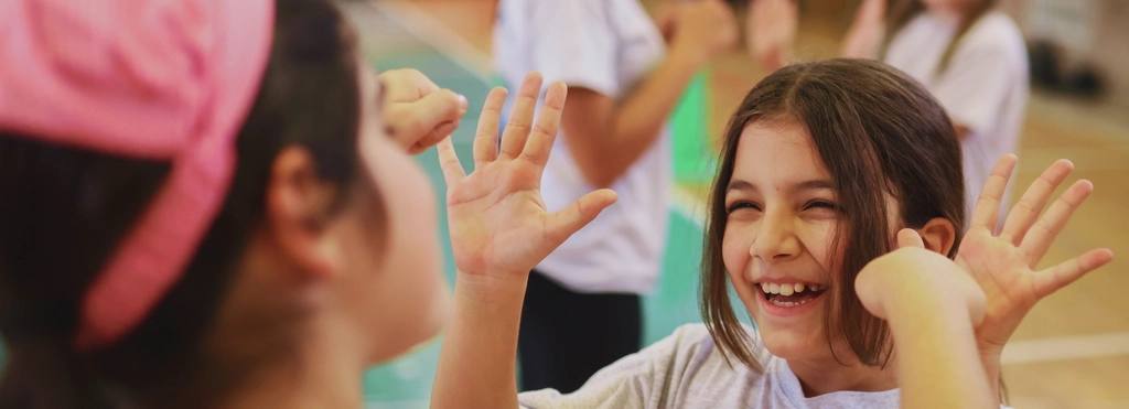 Zwei Mädchen klatschen sich ab bei deinem Sportangebot in einer Turnhalle
