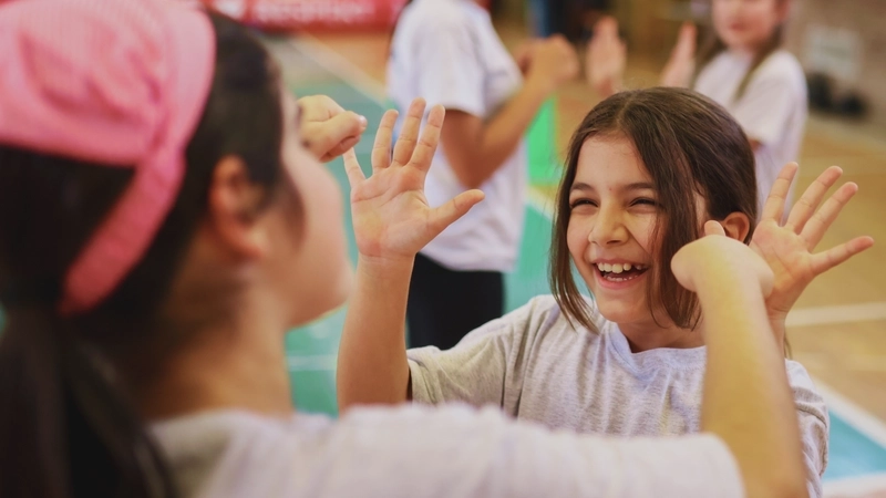 Zwei Mädchen klatschen sich ab bei deinem Sportangebot in einer Turnhalle