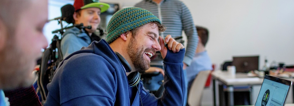 Ein Mann sitzt an einem Laptop und lacht.