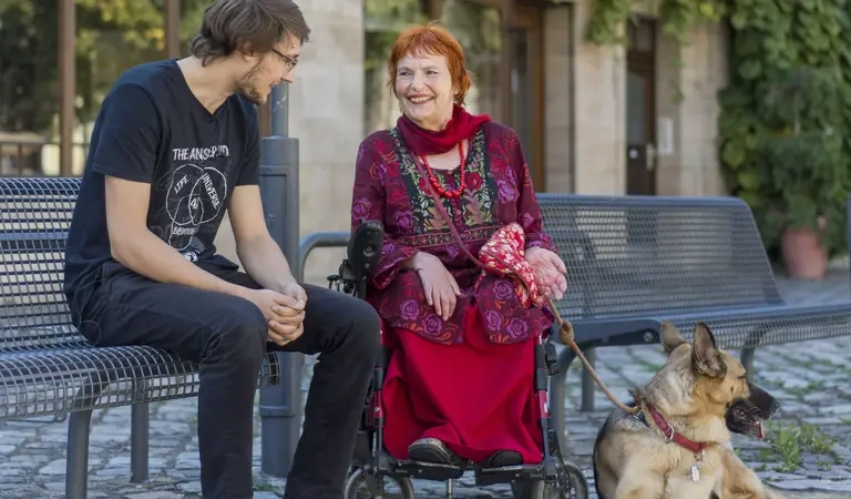 Eine Frau mit Hund und im Rollstuhl unterhält sich mit einem jungen Mann