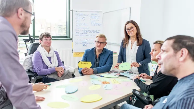 Eine Gruppe von Menschen mit und ohne Behinderung sitzen an einem Tisch und arbeiten gemeinsam,.