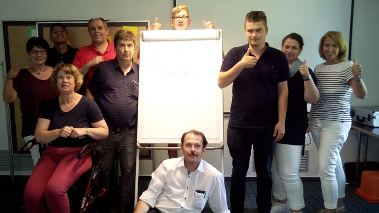 Eine Gruppe Menschen steht um ein Flipchart herumgruppiert