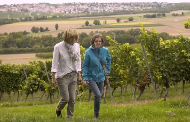 Zwei Frauen laufen einen Berg hoch, im Hintergrund sind Weinreben.