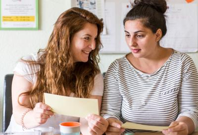 Zwei junge Frauen sitzen nebeneinander, sie erarbeiten etwas auf Papier