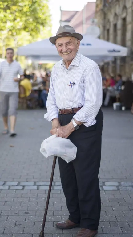 Ein älterer Mann mit einem Stock auf einem Platz lacht