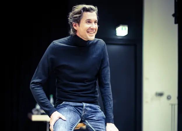 Marcus Brien sitzt auf einem Hocker und lächelt