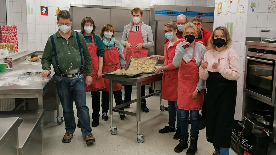 Gruppenbild von Personen, die mit Masken in einer Küche stehen und gebackene Plätzchen zeigen