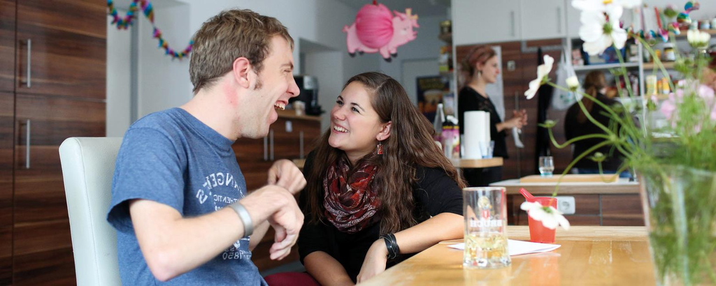 Ein Mann und eine Frau sitzen am Esstisch und lachen gemeinsam.