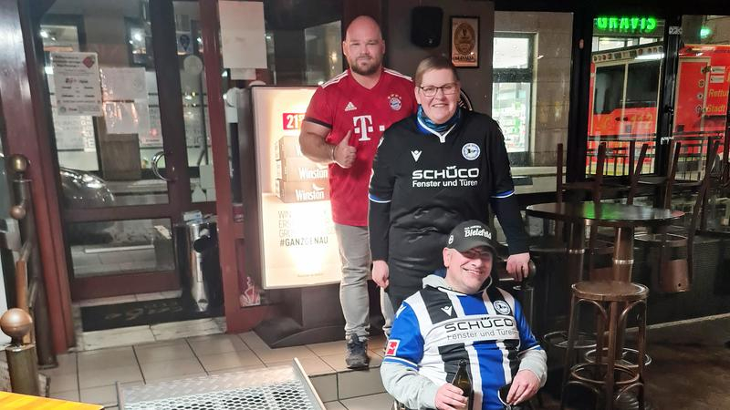 Drei Personen, eine davon im Rollstuhl, neben einer Rampe vor einer Kneipe