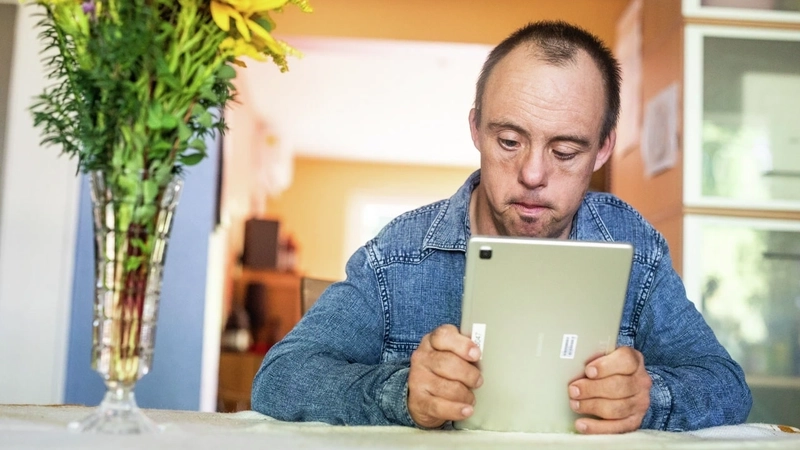 Ein Mann mit Downsyndrom schaut auf ein Tablet.