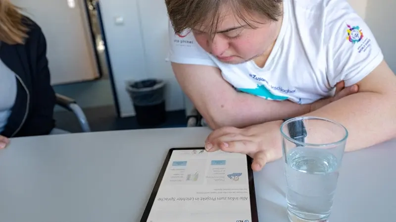 Ein Jugendlicher mit Downsyndrom beugt sich über ein Tablet.