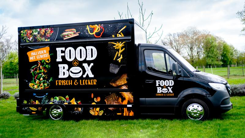 Ein schwarzer LKW mit der Aufschrift Food Box steht auf einer Wiese