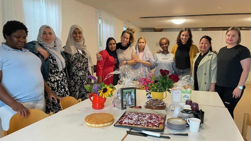 Mehrere Frauen mit und ohne Migrationshintergrund stehen rund um einen Tisch, auf dem Kuchen stehen