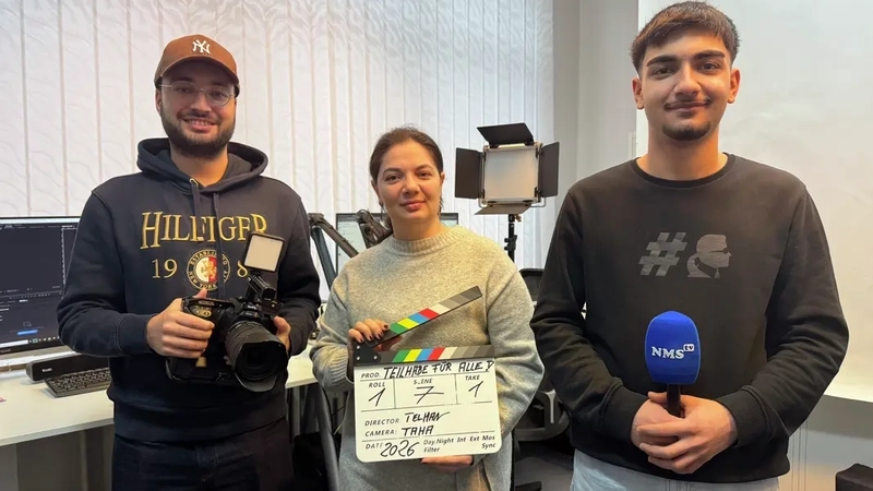 Drei junge Männer und eine junge Frau stehen nebeneinander. Die Frau steht in der Mitte und hält eine Klappe für Filmaufnahmen in den Händen. Der Mann inks von ihr trägt eine Filmkamera. Alle drei haben einen Migrationshintergrund..