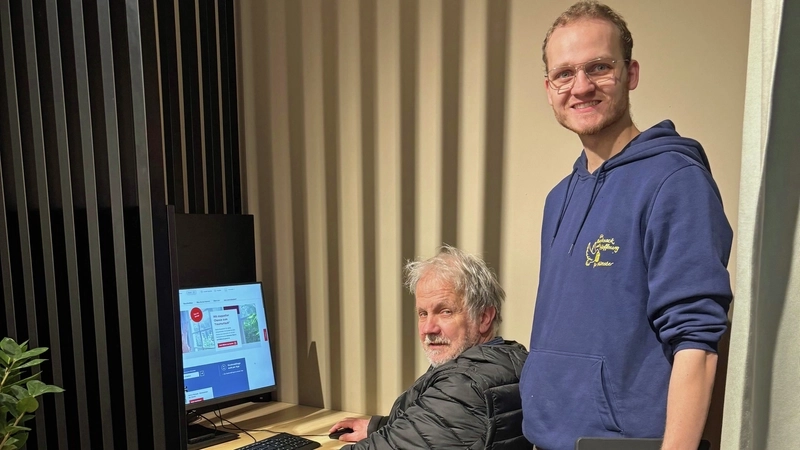 Ein älterer Mann sitzt an einem Computer, ein junger Mann steht neben ihm