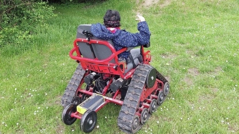 Eine Frau in einem geländefähigen Rollstuhl, von hinten fotografiert.