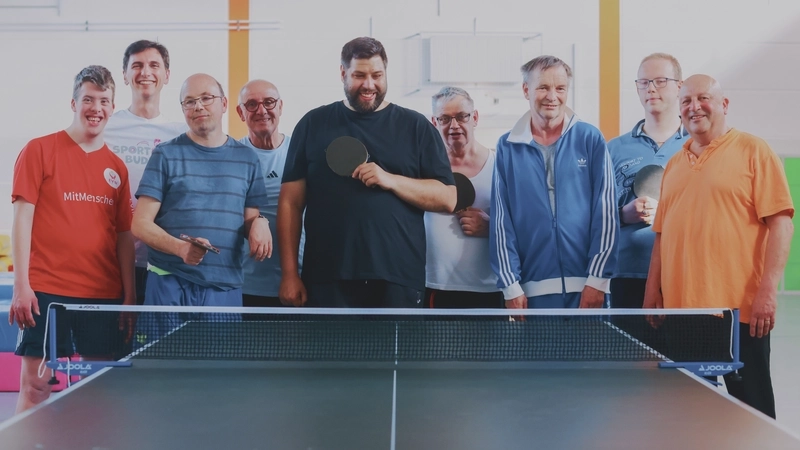Eine Gruppe von Männern mit und ohne Behinderung steht unter einer Tischtennisplatte