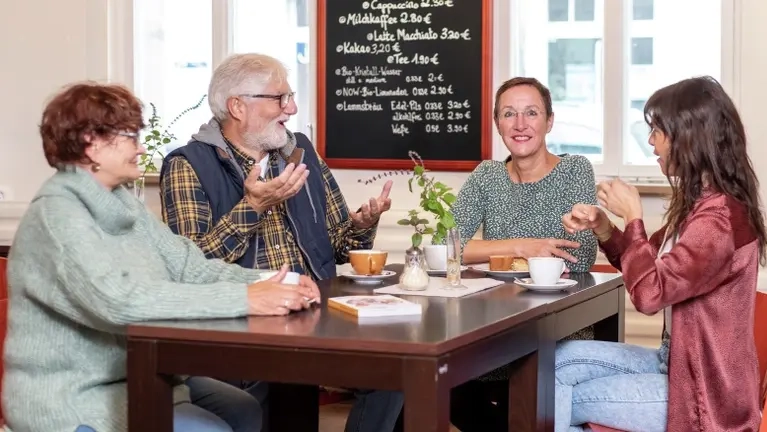 Vier Personen sitzen an einem Tisch und gebärden.